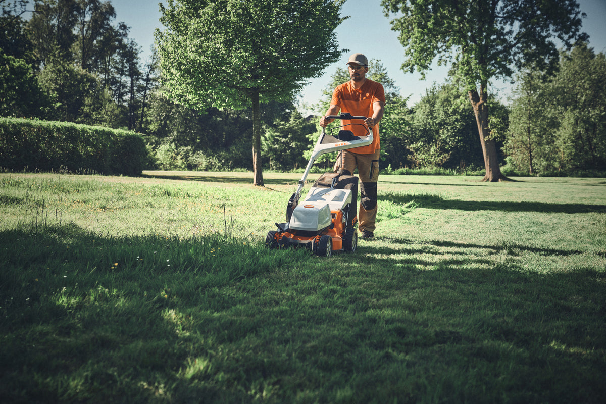 Operatore con tosaerba Stihl su un prato alberato.