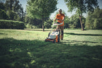 Operatore con tosaerba Stihl su un prato alberato.