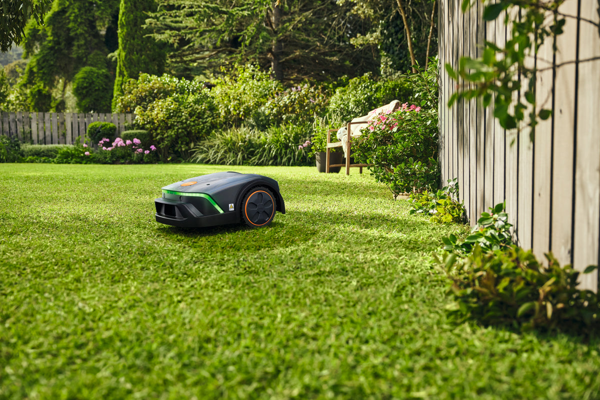 Robot tosaerba Stihl iMOW 4 EVO su un prato vicino a una recinzione e a una panchina.