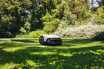 Robot tosaerba Stihl iMOW 4 su un prato circondato da alberi e arbusti.