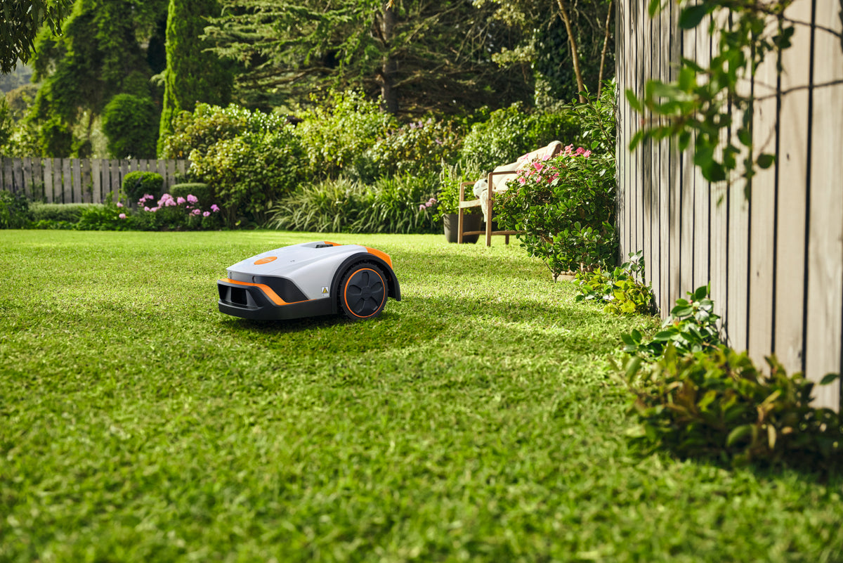 Robot tosaerba Stihl iMOW 4 su prato vicino a una recinzione e a una panca da giardino.