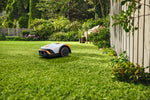 Robot tosaerba Stihl iMOW 4 su prato vicino a una recinzione e a una panca da giardino.