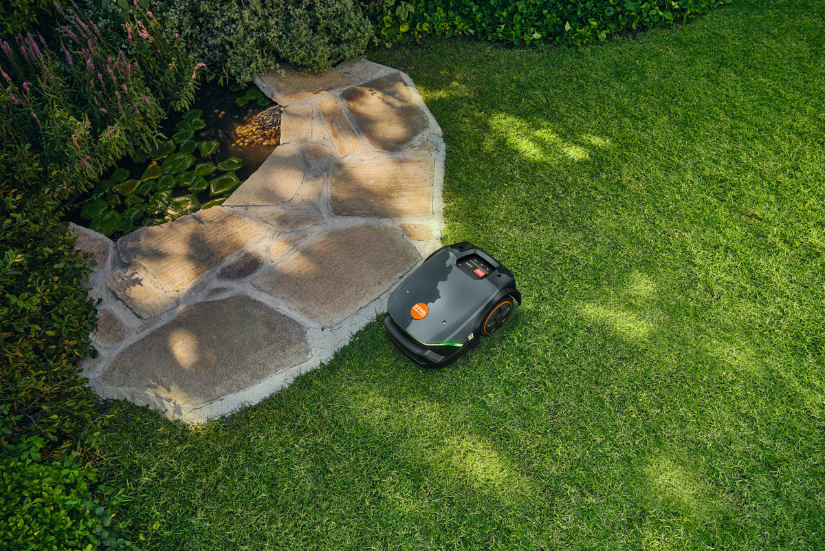 Robot tosaerba Stihl iMOW 4 EVO su prato accanto a un vialetto in pietra.