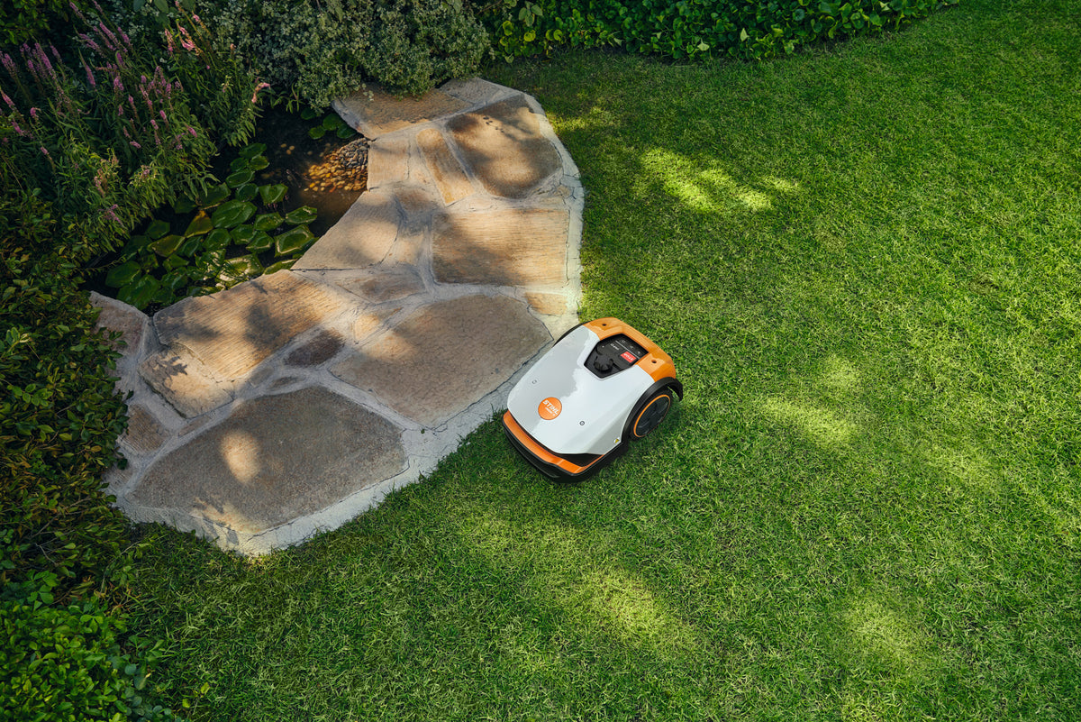 Robot tosaerba Stihl iMOW 4 visto dall'alto su prato accanto a un percorso in pietra.