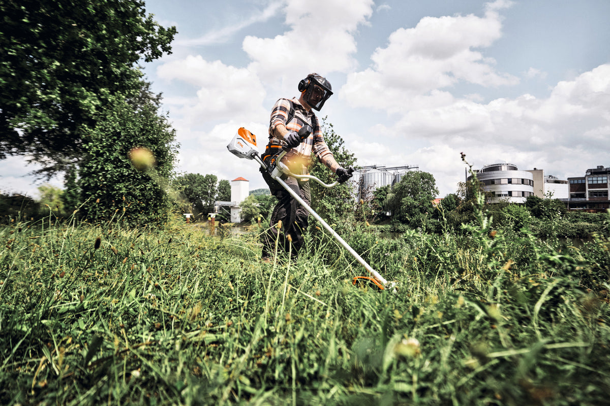 Operatore che utilizza un decespugliatore in un'area con vegetazione alta.