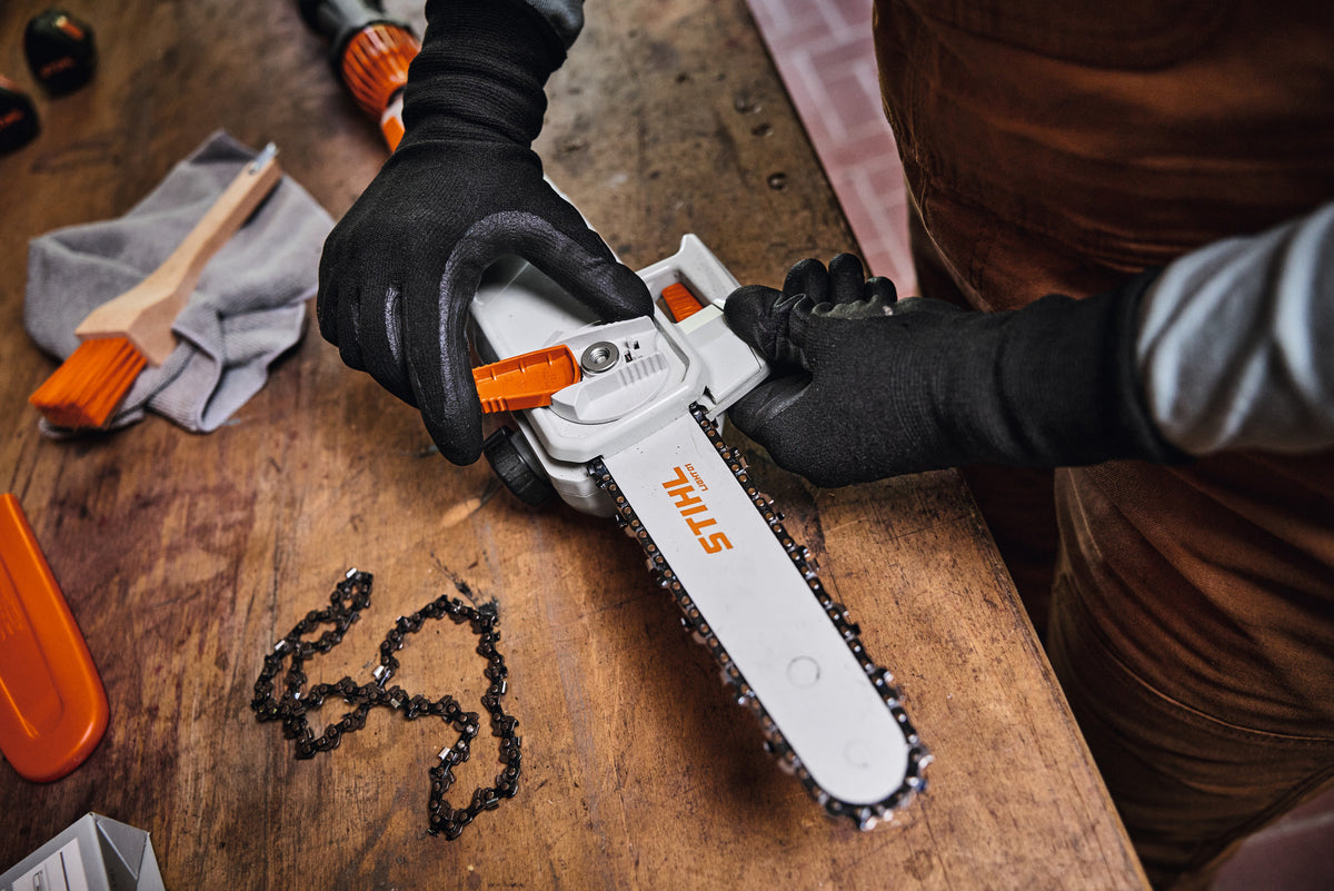 Mani con guanti durante il montaggio della barra e della catena del potatore Stihl HTA 30