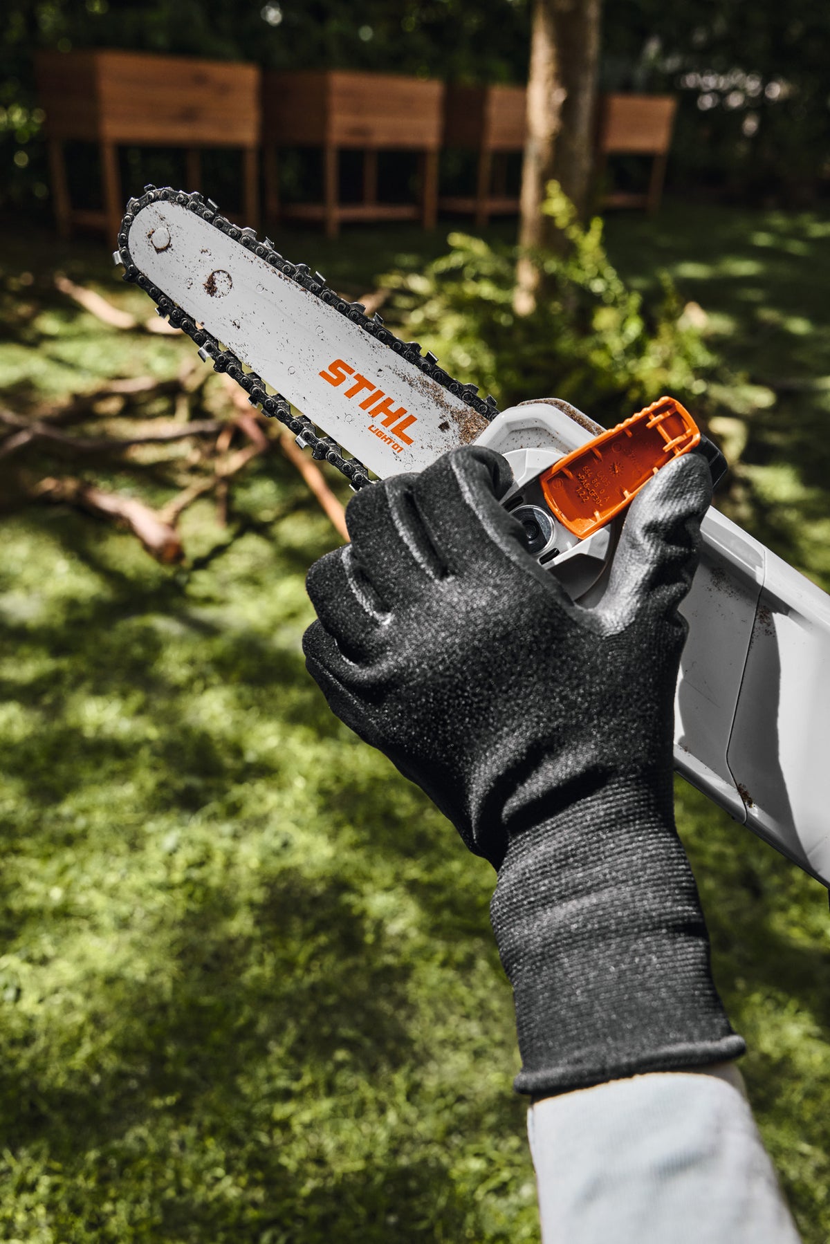 Mani con guanti che regolano il tensionamento della catena del potatore Stihl HTA 30