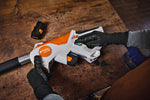 Mani con guanti sul vano batterie del potatore telescopico Stihl HTA 30